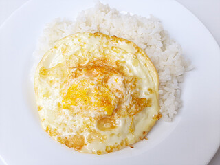 Fried egg or overcooked sunny side up, served with white rice, on a white plate, isolated in white background