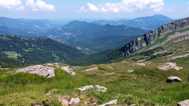 sorvolando uno sperone di roccia e vegetazione sulla cima della montagna fino alla vallata con piccolo lago e montagne all'orizzonte con cielo sereno con nuvole in una giornata d'estate