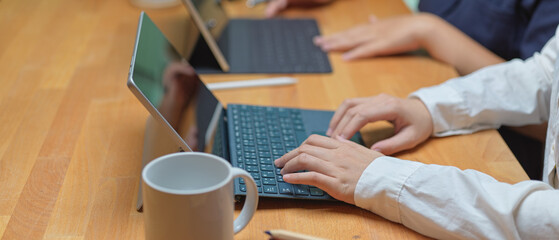 Female worker typing on digital tablet while sitting with her colleague at co working space