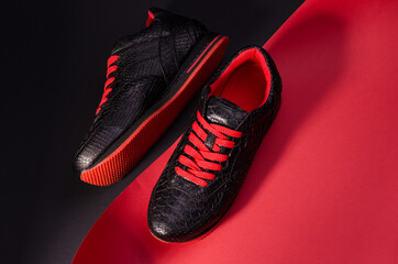 Fashionable snakeskin leather sneakers. Black sneakers with bright red bootlaces against a black...