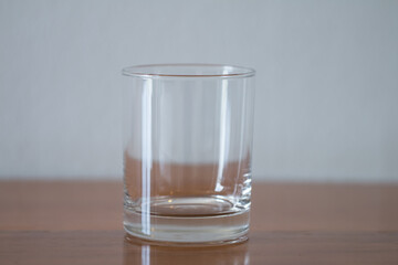 The glass of drinking water is transparent, empty, placed on a brown wooden table. The image is partially clear.