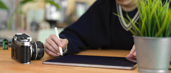 Female using digital tablet on wooden table with camera and tree pot