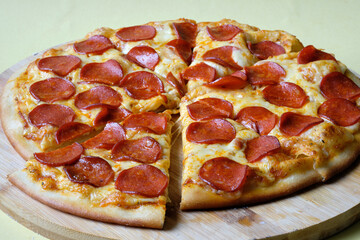 Pizza Pepperoni pieces with sausage slices, chili sauce and mozzarella cheese on the wooden dish. Yellow background. 
