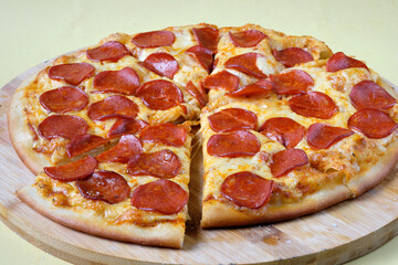Pizza Pepperoni pieces with sausage slices, chili sauce and mozzarella cheese on the wooden dish. Yellow background. 