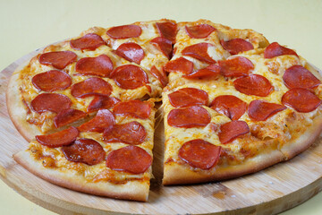 Pizza Pepperoni pieces with sausage slices, chili sauce and mozzarella cheese on the wooden dish. Yellow background. .