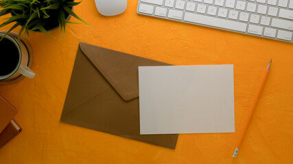 Mock-up greeting card with brown envelope on creative worktable with computer keyboard and decorations
