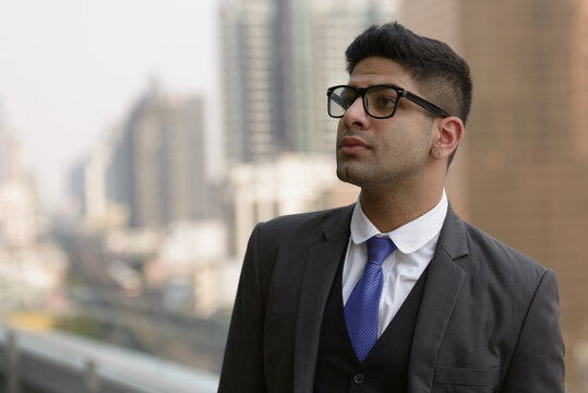 Young handsome Indian businessman with eyeglasses thinking in the city