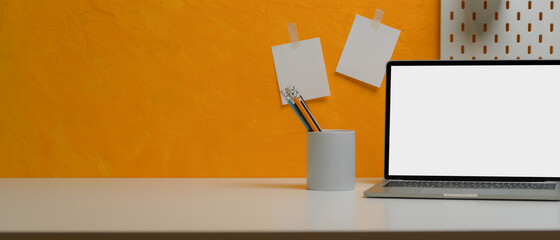 Creative home office desk with mock-up laptop, stationery, copy space and notepad on yellow wall