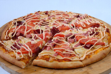 Sliced Pizza with mozzarella, tomatoes, mayonnaise and sausages on wooden board. Blue background. Delicious Italian food. Cafe, pizzeria and restaurant menu. 