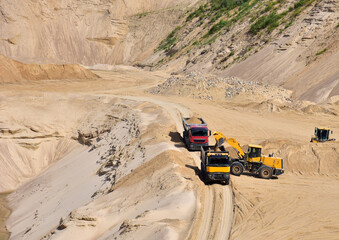 Wheel front-end loader loading sand into heavy dump truck at the opencast mining quarry. Dump truck transports sand in open pit mine. Quarry in which sand and gravel is excavated from the ground.