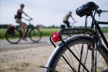Fototapeta premium Two blurry cyclists cycle past a parked bicycle on a country road on a summer day. Focus on mudguard with red rear light