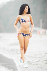 Beautiful smiling young woman with american flag on the beach on independence day