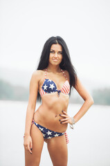 Beautiful smiling young woman with american flag on the beach on independence day