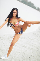 Fototapeta premium A woman in a swimsuit with an American flag walks along the coast