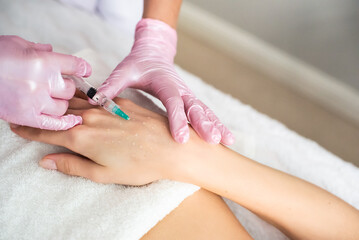 Hand skin biorevitalization. in the cosmetologist’s office, an injection in the wrist. pink gloves, a white towel.