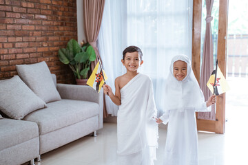 cute little kid wearing muslim ihram clothes and dress. hajj and umrah concept with brunei flag