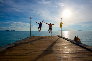 two people jump from the pier into the water, feel freedom, have fun traveling in the tropics, jump...