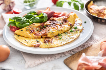 Omelette with prosciutto peas basil tomatoes and herbs on white plate