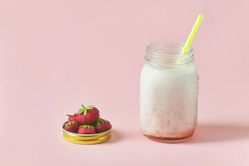 milk strawberry smoothie on pink background. handful of ripe strawberries in a jar lid