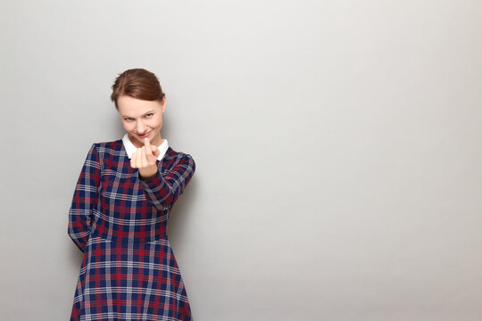 Portrait of cheerful girl beckoning someone with finger and smiling