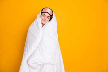 Photo of cheerful lady satisfied enjoy morning hug warm blanket eyes closed joyful facial expression wear mask white plaid pajama pants isolated yellow color background