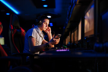 Young gamer looking at smart phone at cybercafe, copy space, portrait.