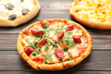 Three different kinds of pizzas on brown wooden table with copy space