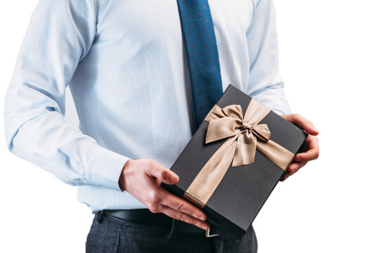 A man holds a gift in his hands with a golden ribbon. Guy on a white background in a light shirt with a tie. Black gift box in the hands..