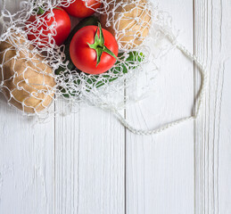 Vegetables in a string bag on a white wooden table. Space for text. The view from the top