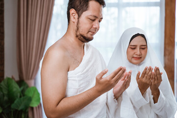 Muslim couple praying open their arm wearing ihram