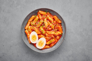 Tteokbokki with eggs in gray bowl on concrete table top. Tteok-bokki is a korean cuisine dish with rice cakes. Asian food. Top view