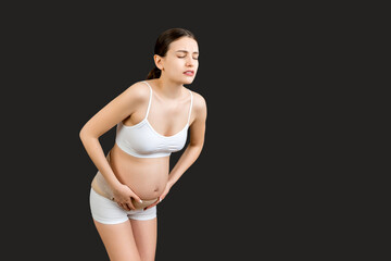 Fototapeta na wymiar Portrait of supporting bandage against backache on pregnant woman in underwear at black background with copy space. Mother is suffering from pain in the back. Orthopedic abdominal support belt concept