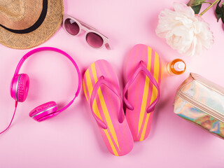 Summer beach vacation concept on pink background with hat, pair of flip flops, sunglasses, headphones and sun protection spray