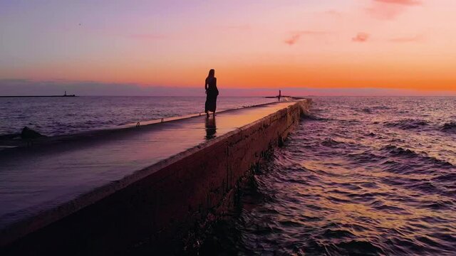 Amazing aerial view of young walking woman at rocky pier with beautiful waves of Baltic Sea Gulf in background