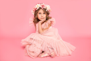 Studio photo of a small beautiful girl with a wreath of flowers on her head and curls of hair. Background, accessories, pink dress. Hairdressing salon. Children's cosmetic.