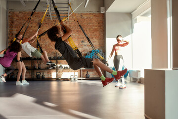 Portrait of teenage kids having fun while training using fitness straps in gym with female trainer....