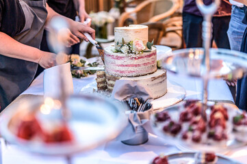 cutting a beautiful delicious Wedding cake in many tiers with fresh wild flowers and roses