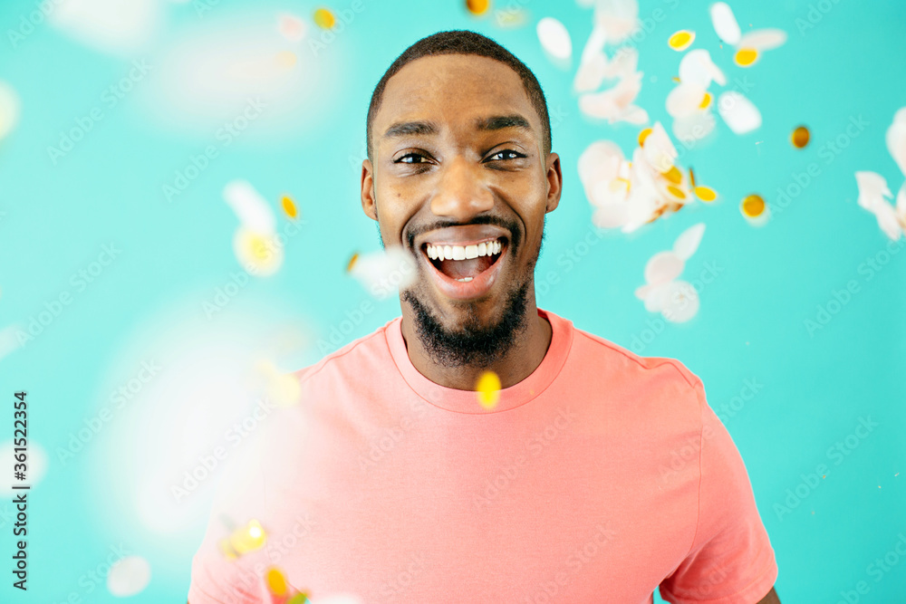 Wall mural Portrait of a cheerful black man laughing looking at camera with confetti falling around