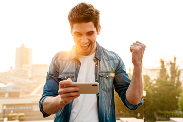 Photo of man making winner gesture and playing game on cellphone