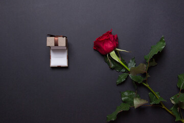 sngle red rose and open brown jewelery box on black colored paper background, with copy space