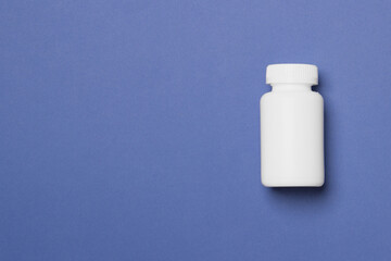 White plastic medical container for pills on right side of blue colored paper background with copy space