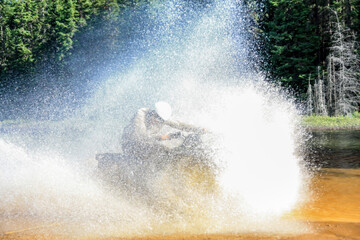 Man driving motocross ATV quad through splashing river lake water with high speed. Foy, Foyross Lake, Sudbury, Canada.