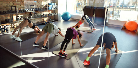 Experience the joy of yoga. Full-length shot of kids doing yoga exercises together with female trainer in gym. Stretching on a sunny day. Sport, healthy life, physical education concept