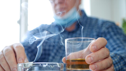 Man Wearing Protection Mask on His Face Drink a Glass with Alcohol in a Bar and Smoke a Cigarette
