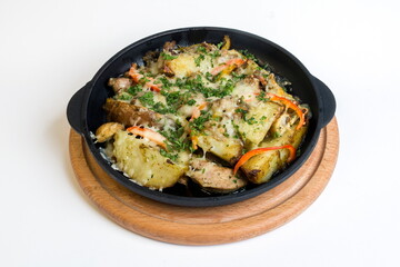 Dish on a black pan, which stands on a wooden stand. Baked potatoes with meat red and yellow pepper. Sprinkled with green parsley.