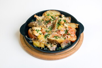 Dish on a black pan, which stands on a wooden stand. Baked potato with bacon red pepper and tomato. Sprinkled with green parsley.