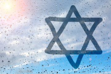 Figure eight-pointed star, a symbol of Judaism, on wet glass. Glass window with raindrops against...