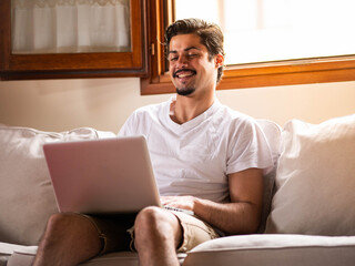 A picture of a brunette male sitting on a white sofa with a laptop
