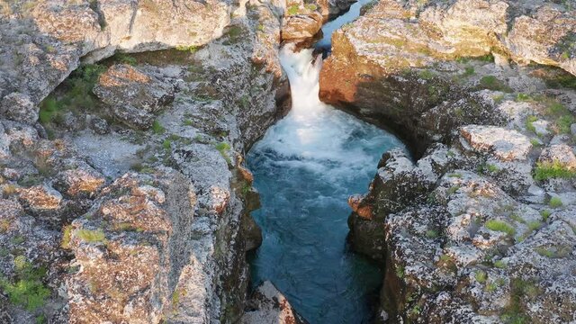 Waterfall on a narrow blue mountain river flowing through rocky landscape. Stream bed cut deep into stones. Upstream of Cijevna (Cem) in Montenegro. Aerial footage.