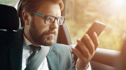 Close-up of serious businessman looking at smartphone screen sitting in car during road trip
